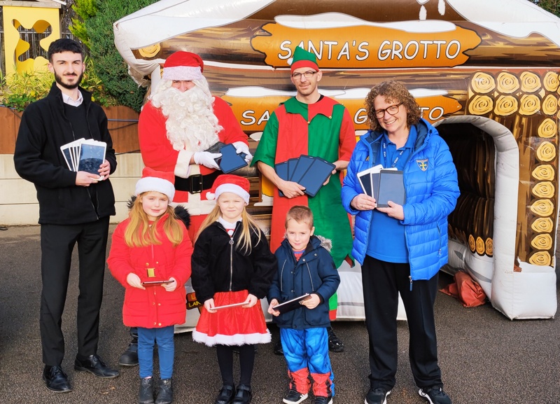 Adam Wozniak (left) presents the tablet computers to headteacher Mair Hindmarsh (right) watched by pupils at Kirkby C of E Primary School, together with Santa and an elf